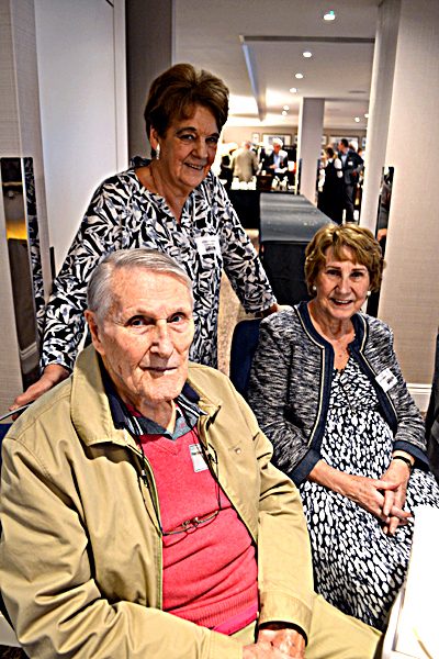 A guest seated with two women standing behind him